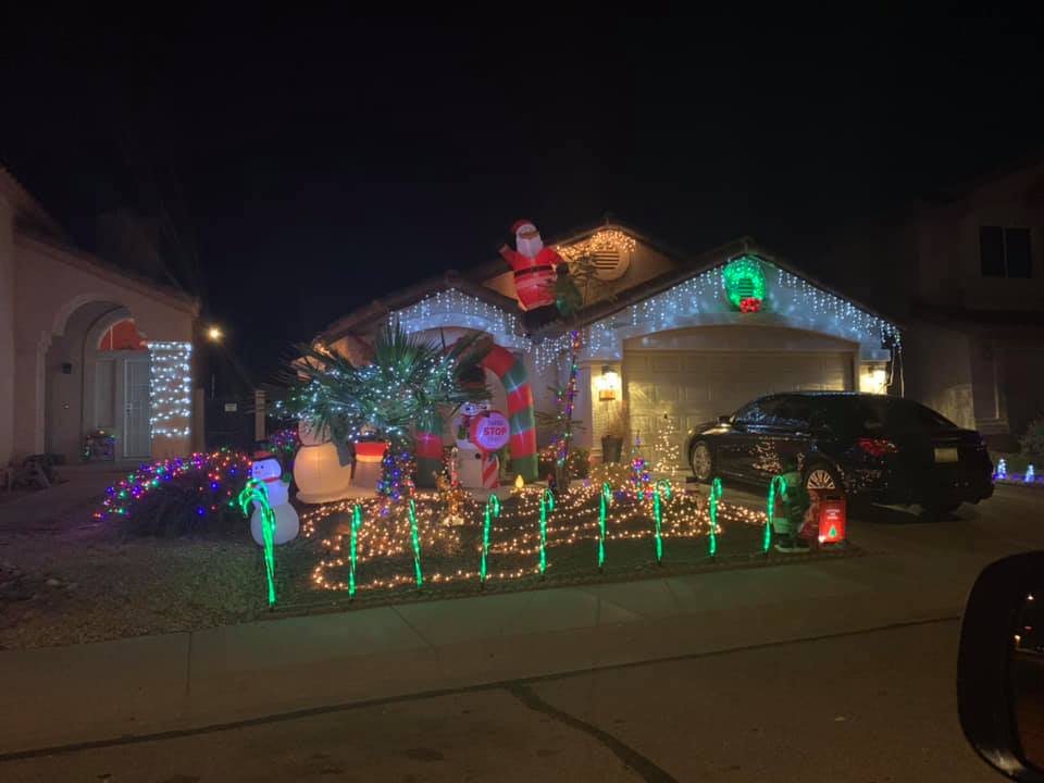 House covered in colorful Christmas lights at night, with a Santa figure on the roof and a car in the driveway