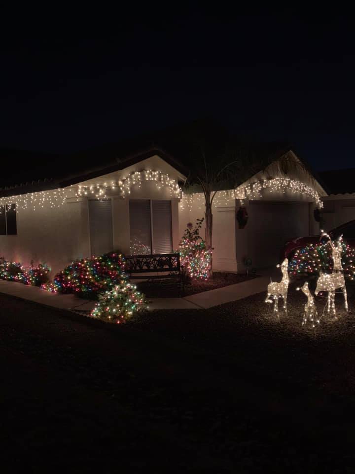House decorated with Christmas lights, wreaths, and illuminated reindeer in the front yard at night
