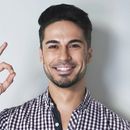 Smiling man in a checkered shirt waving against a light gray background